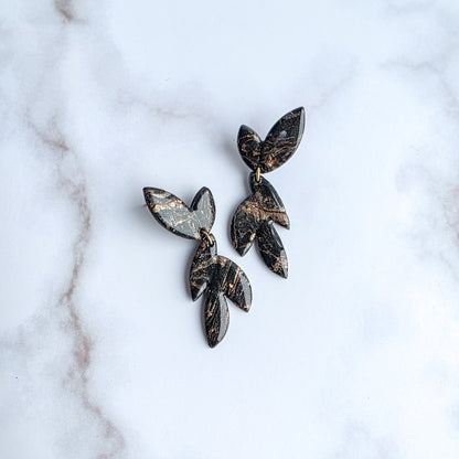 bladvormige marmer zwarte oorbellen in geschilderde metallic kleuren op wit grijs marmeren blad