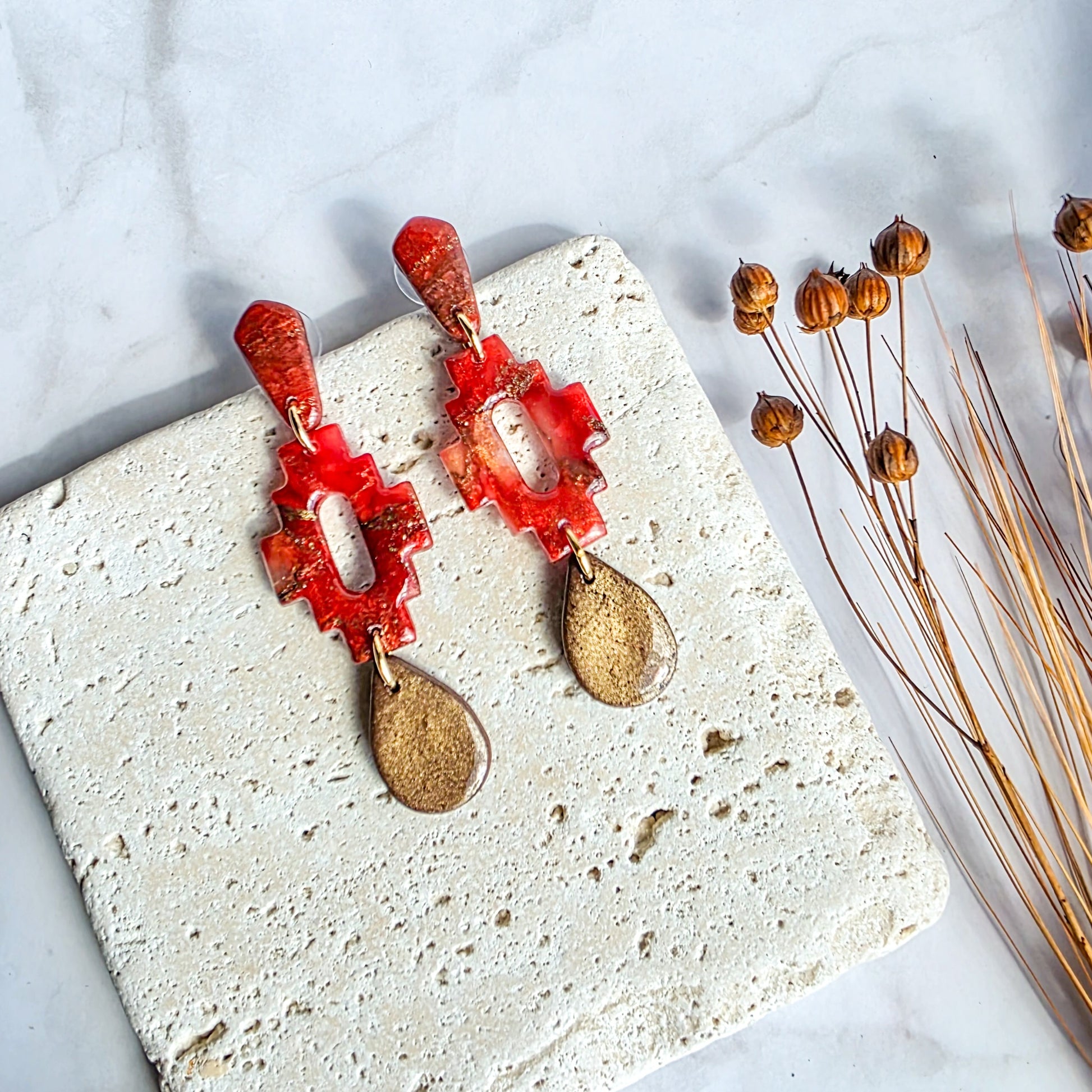 Lange steenrode oorbel met bronskleurige druppel