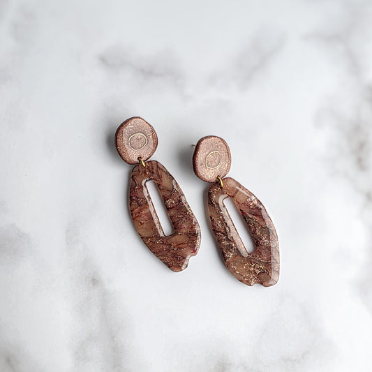 Lange bruine oorbellen met gouden spikkel en rond oorknopje op wit grijs marmeren blad