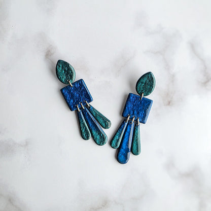 lange blauwe metallic statement oorbellen met groen metallic op wit grijs marmeren blad