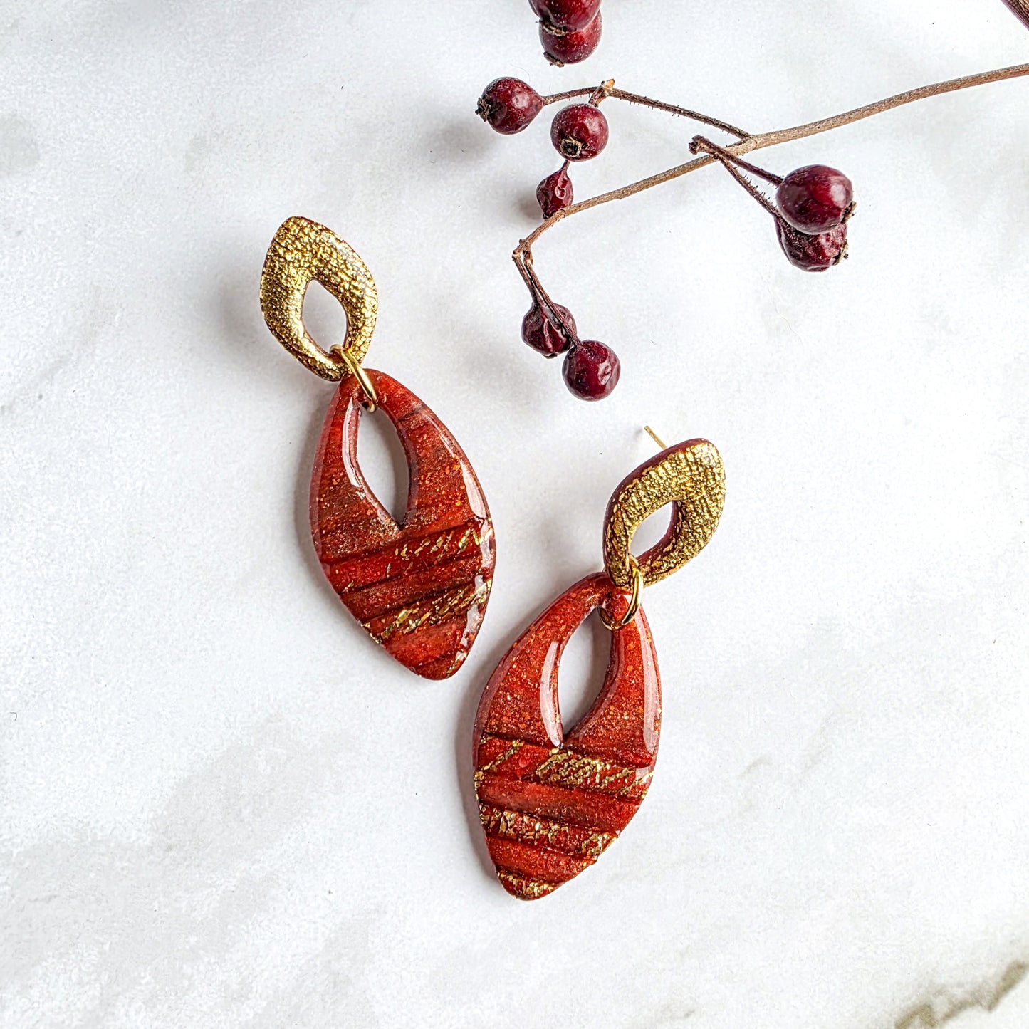 Unieke handgemaakte lange oorbellen in goud en steenrood, gemaakt van polymeerklei – Handmade Elegance by Delfine