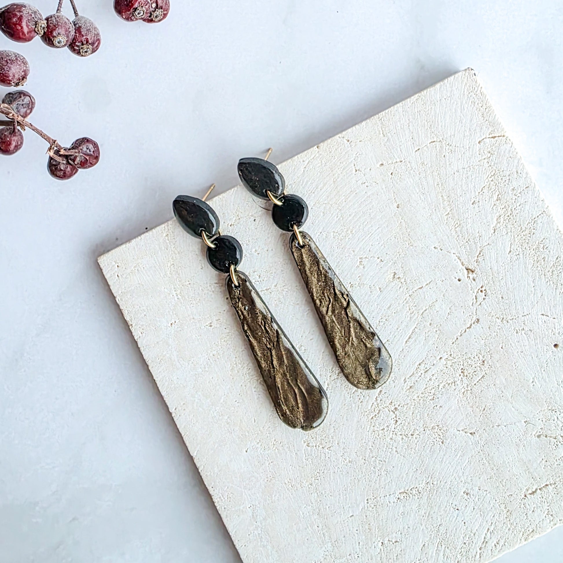 lange bronskleurige oorbellen met zwart oorknopje op marmeren blad met takje