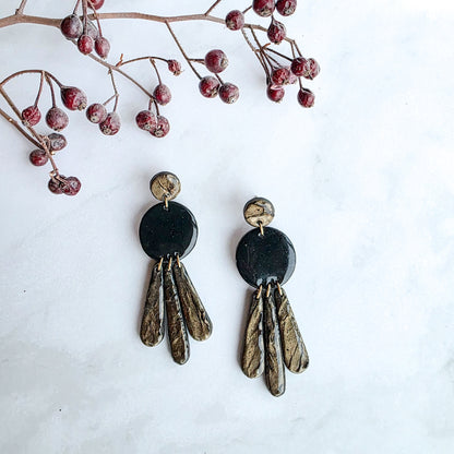 lange zwarte oorbellen met bronskleurige slingers en oorknopje op marmeren blad met takje