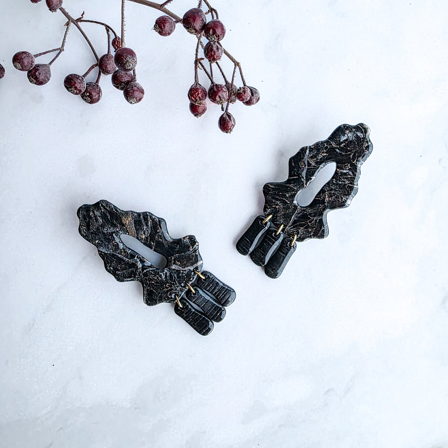 zwarte marmeren oorbellen met goud op marmeren blad met takje