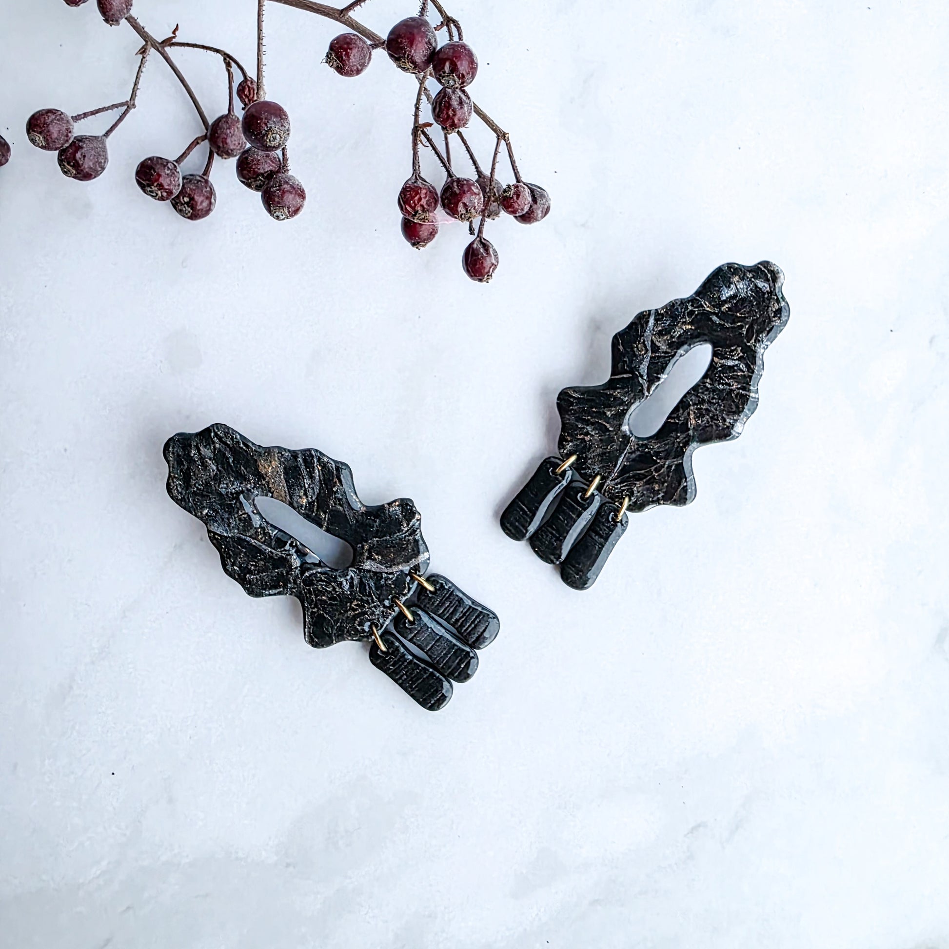 zwarte marmeren oorbellen met goud op marmeren blad met takje