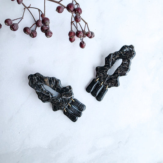 zwarte marmeren oorbellen met goud op marmeren blad met takje