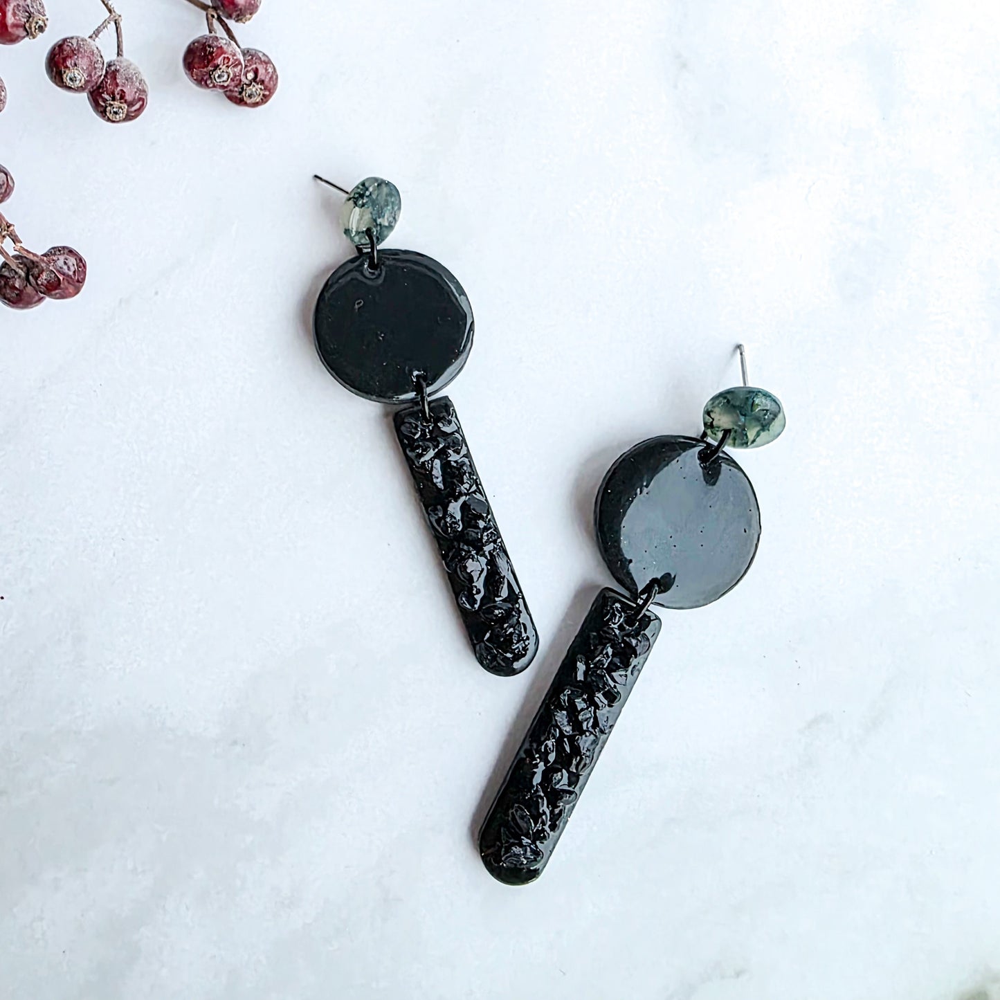 lange zwarte oorbellen met groen oorknopje en zwarte blinkers op marmeren blad met takje