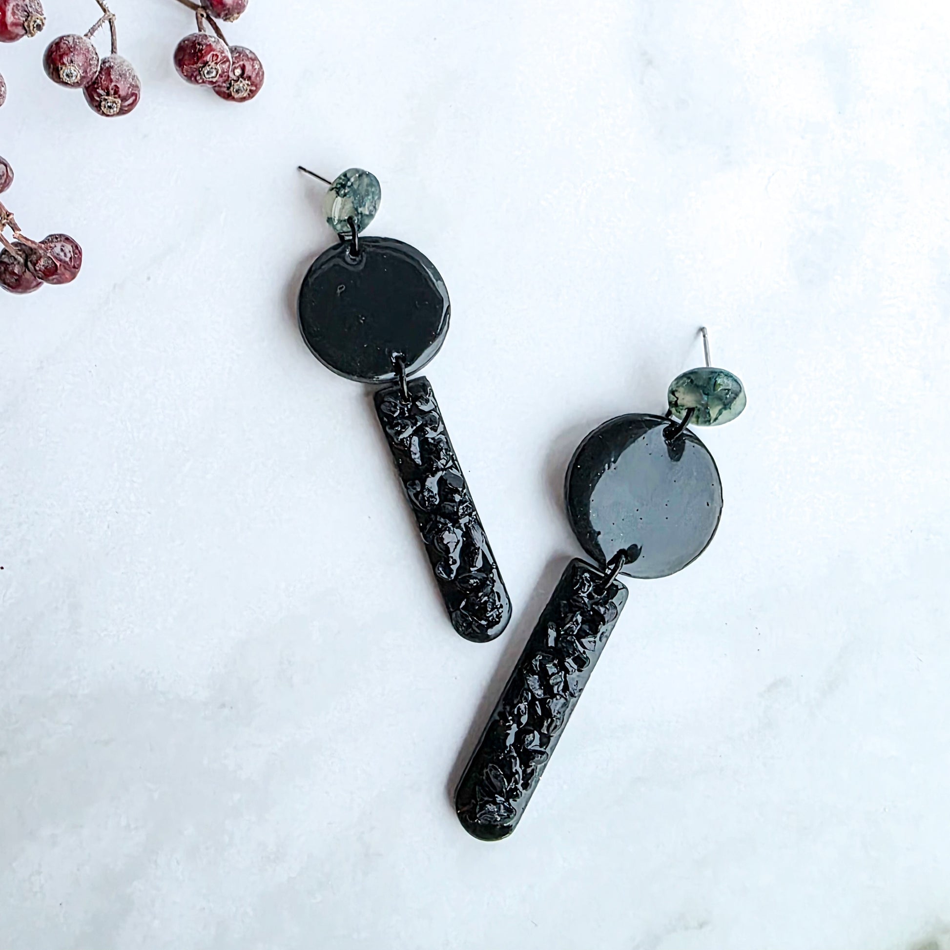 lange zwarte oorbellen met groen oorknopje en zwarte blinkers op marmeren blad met takje