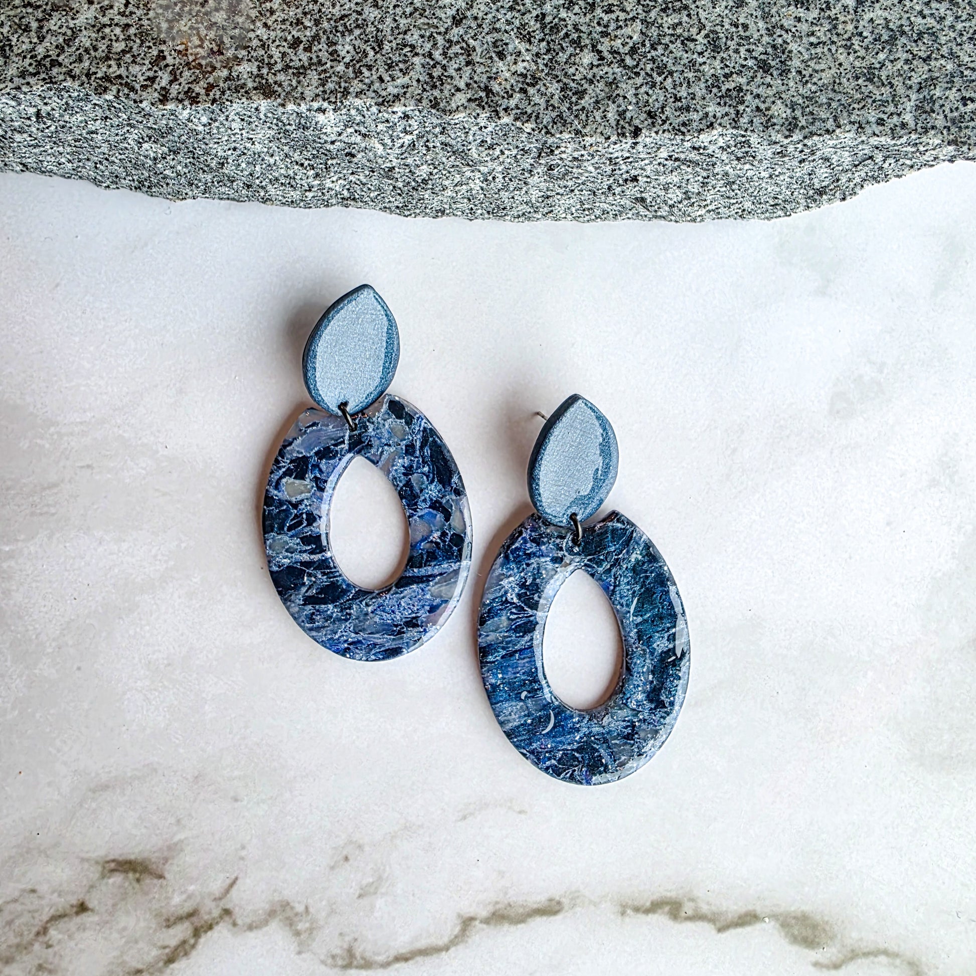 lange koel blauwe oorbellen op wit grijs marmeren blad met granieten steen