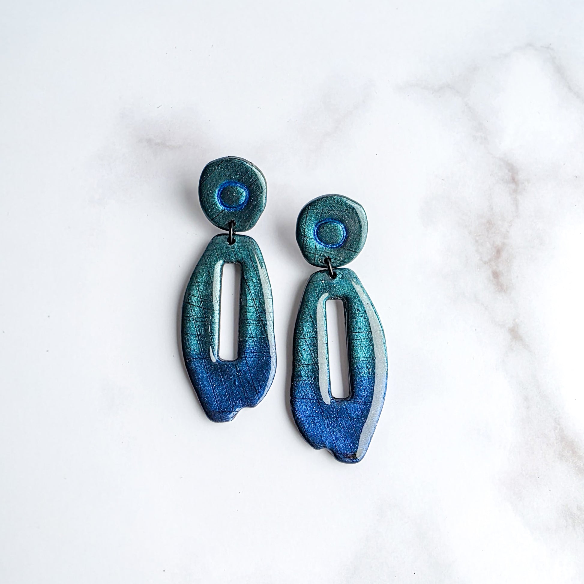 lange blauwe metallic oorbellen met groed metallic op wit grijs marmeren blad