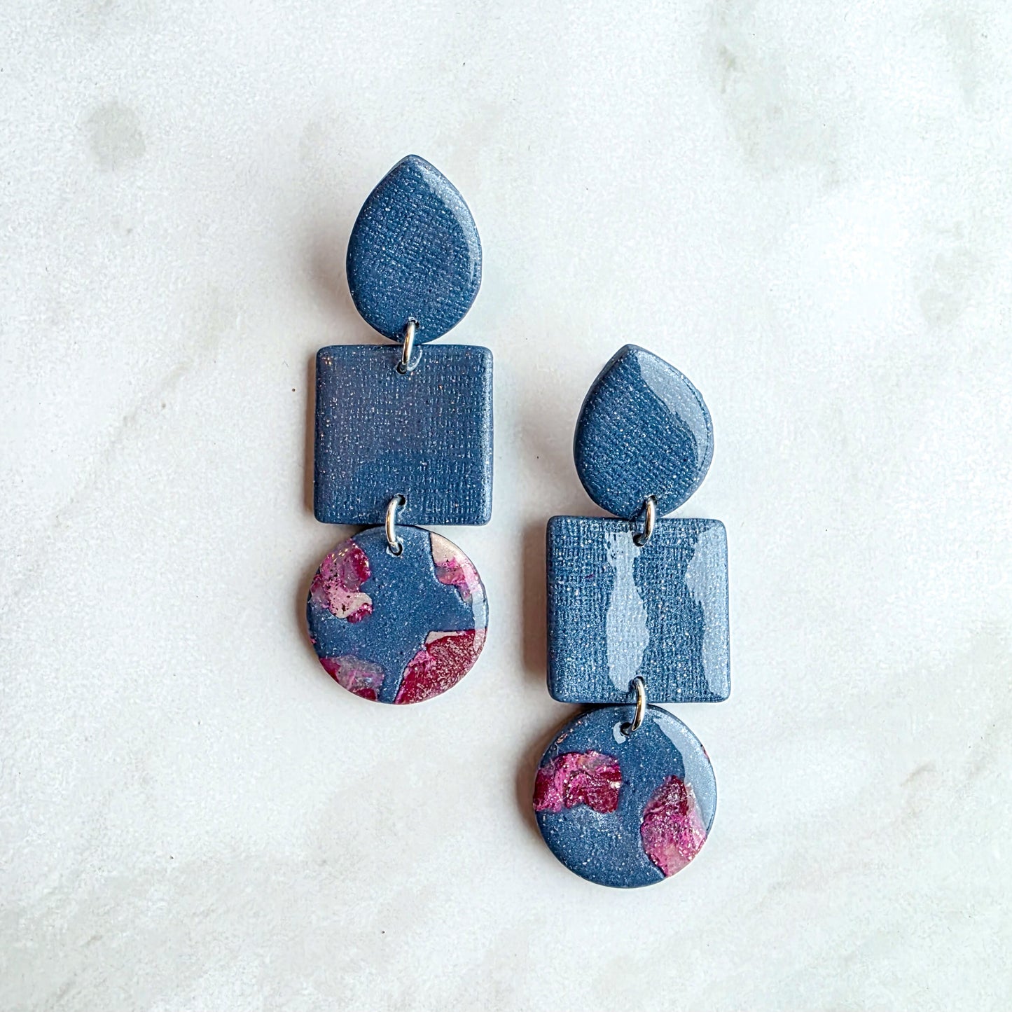 Druppelvormige jeansblauwe oorbellen met burgundy red op wit grijs marmeren blad