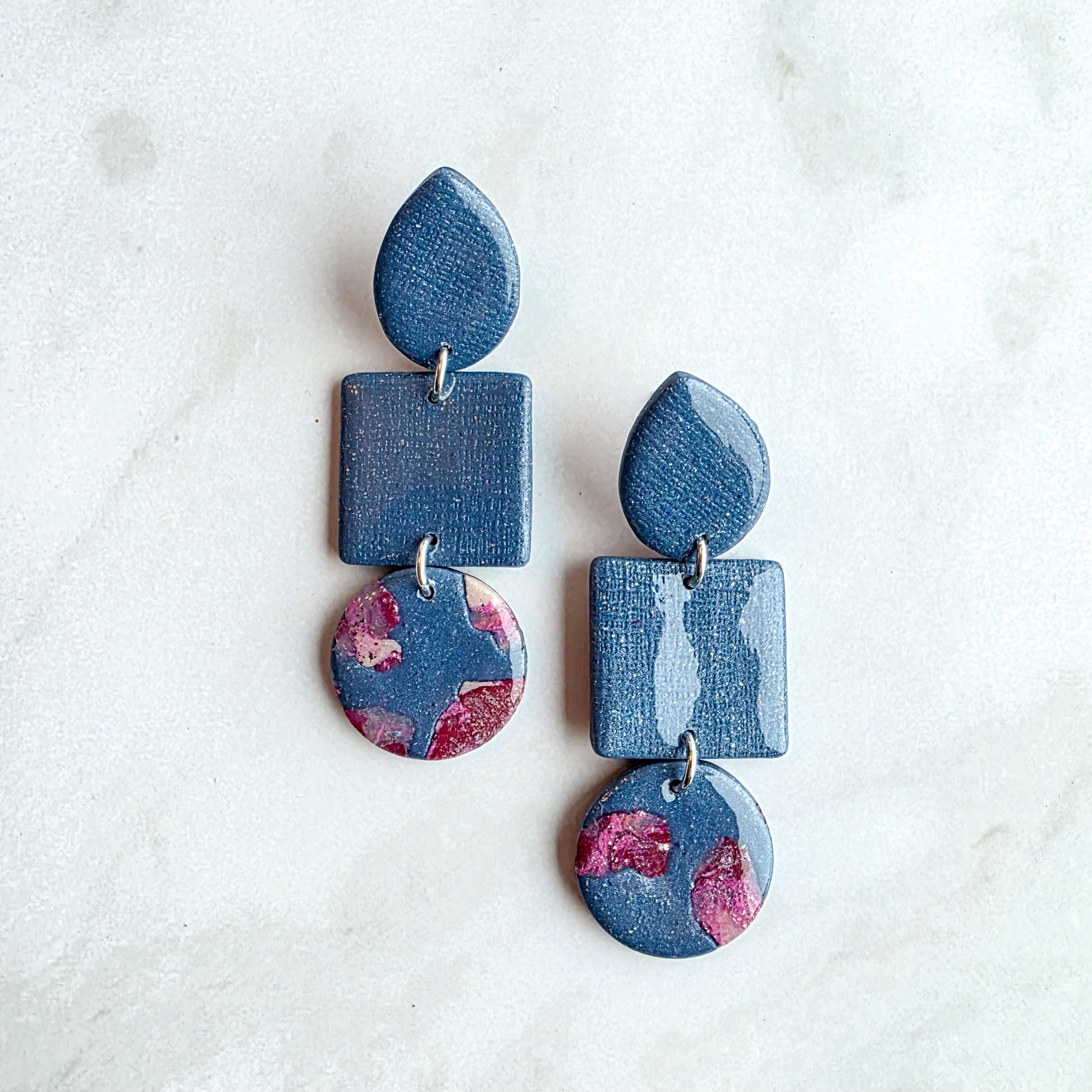 Druppelvormige jeansblauwe oorbellen met burgundy red op wit grijs marmeren blad