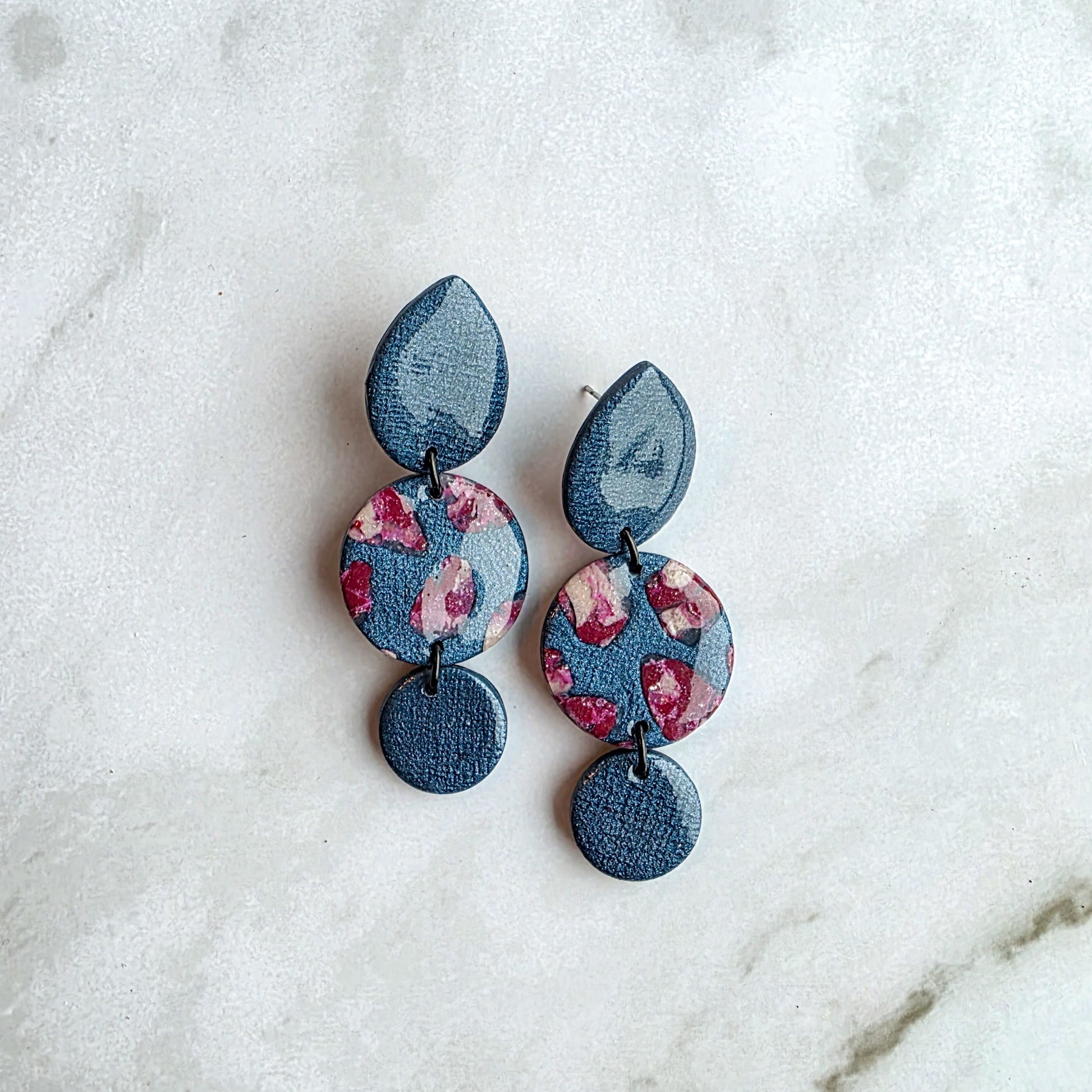 Omgekeerde druppelvormige jeansblauwe oorbellen met burgundy red op wit grijs marmeren blad