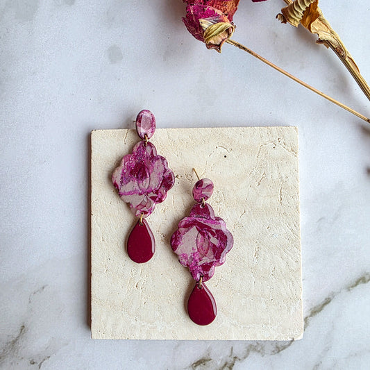 lange burgundy red bloemvormige oorbellen op wit grijs marmeren blad met roze gedroogde bloem