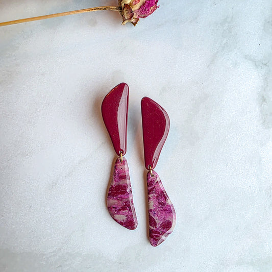 lange burgundy red oorbellen op wit grijs marmeren blad met roze gedroogde bloem