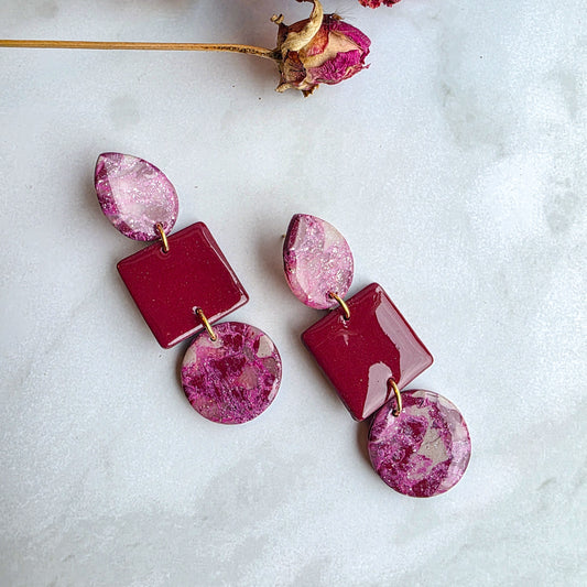 lange burgundy red statement oorbellen op wit grijs marmeren blad met roze gedroogde bloem