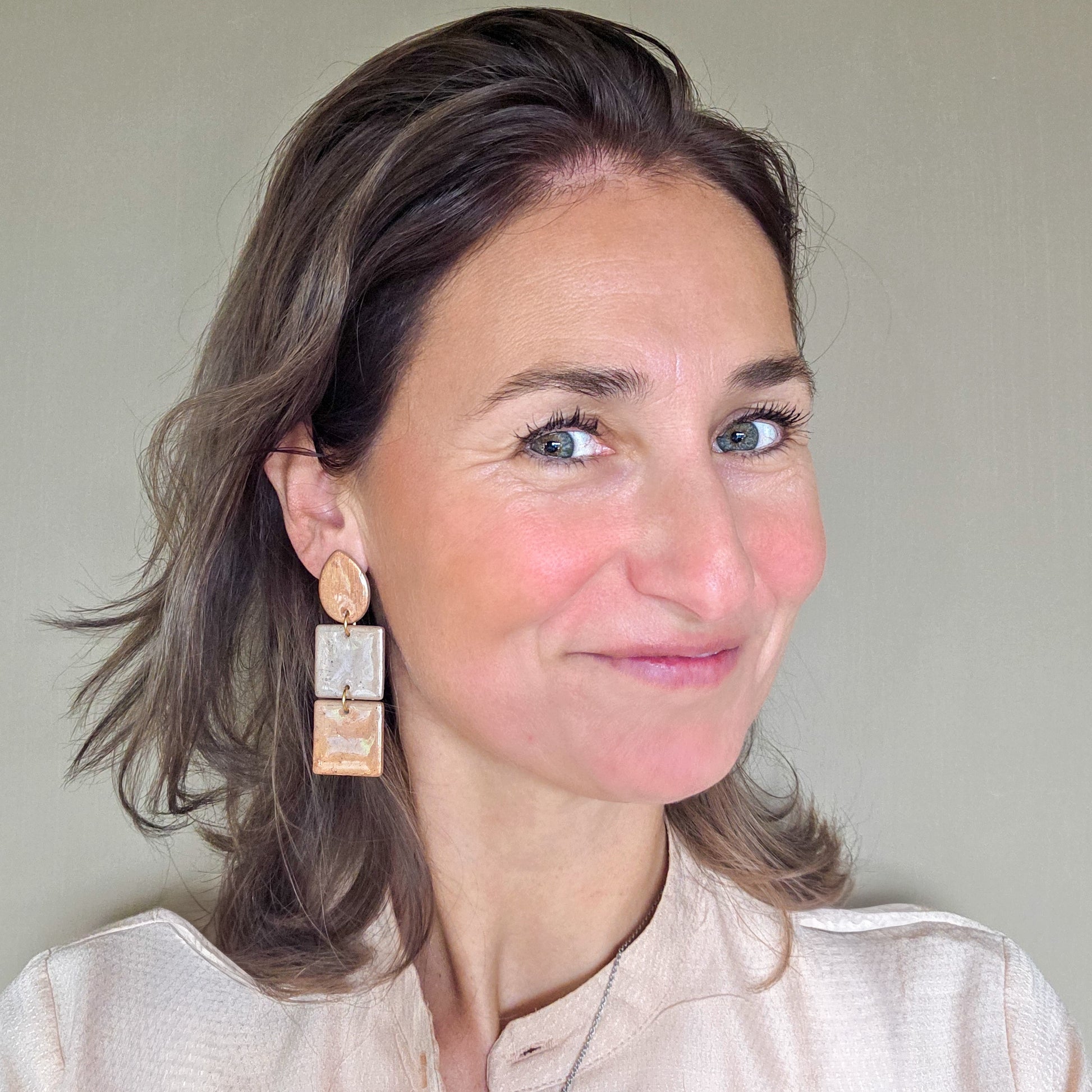 vrouw draagt lange metallic statement oorbellen met druppelvormig oorknopje in  goud en koper metallic kleuren