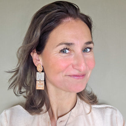 vrouw draagt lange metallic statement oorbellen met druppelvormig oorknopje in  goud en koper metallic kleuren