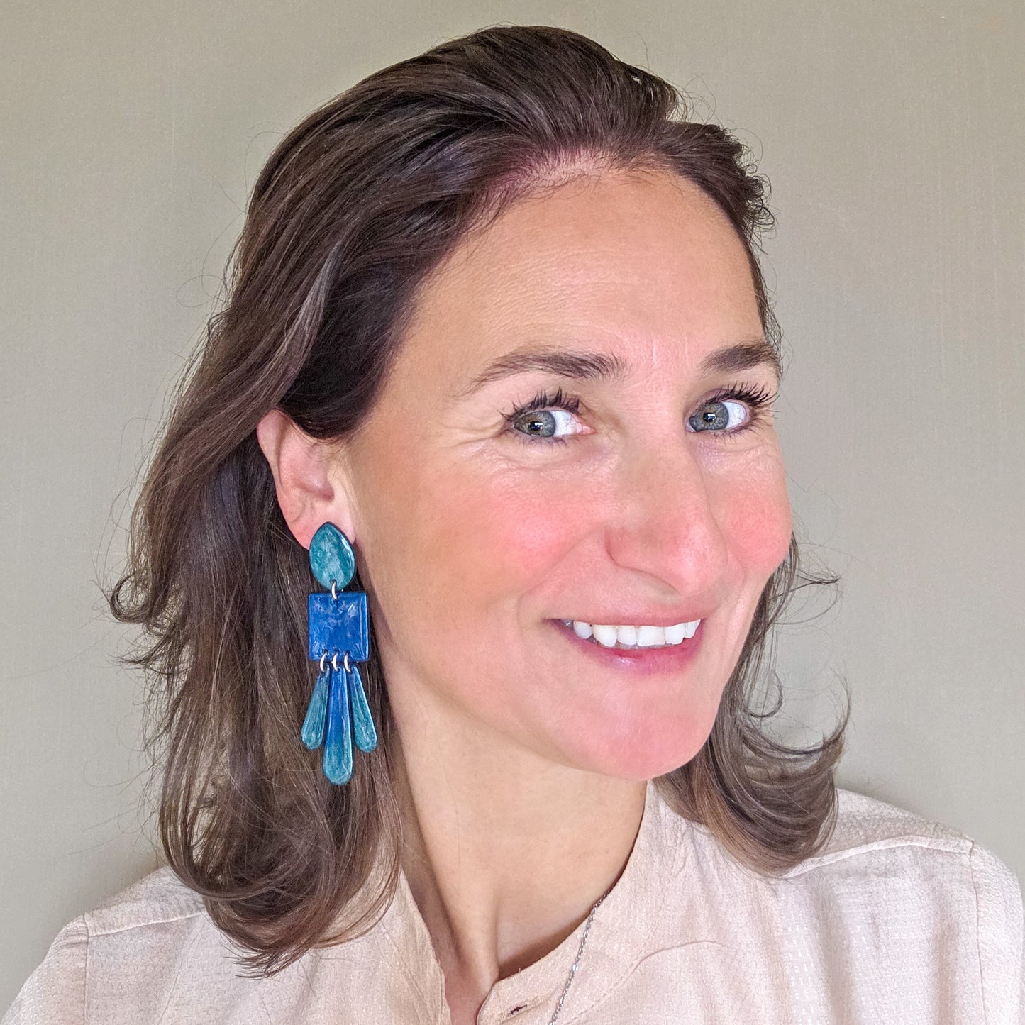 vrouw draagt lange statement oorbellen in metallic groen en blauw met slingers