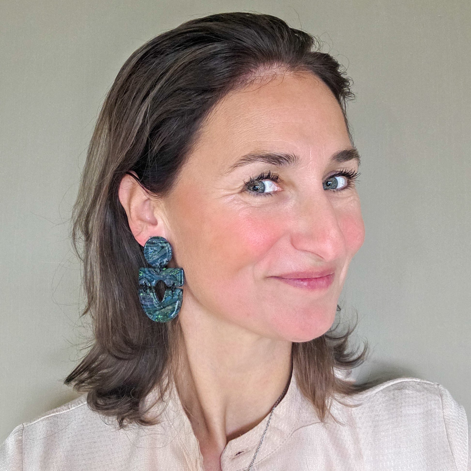 vrouw draagt lange zwarte met groene statement oorbellen met metallic spikkel