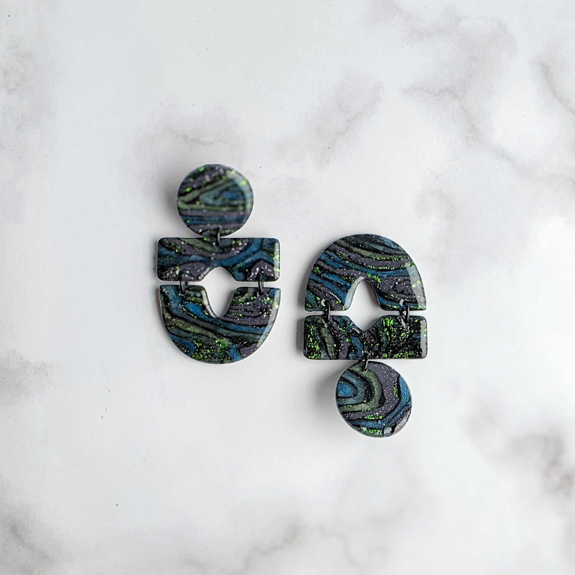 statement oorbellen met groen, zwart en grijs en groene metallic spikkels op wit grijs marmeren blad