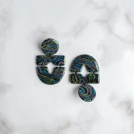 statement oorbellen met groen, zwart en grijs en groene metallic spikkels op wit grijs marmeren blad