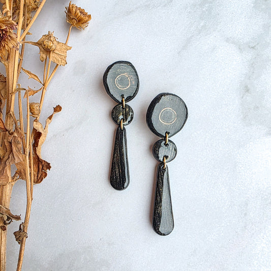lange zwarte met goudkleurige oorbellen op wit grijs marmeren blad met takje