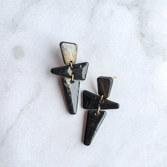 kleine zwarte met goudkleurige hoekige oorbellen op wit grijs marmeren blad