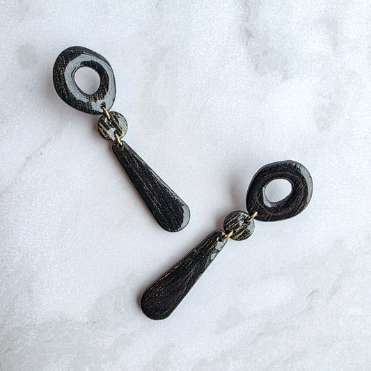 lange zwarte met goudkleurige oorbellen op wit grijs marmeren blad